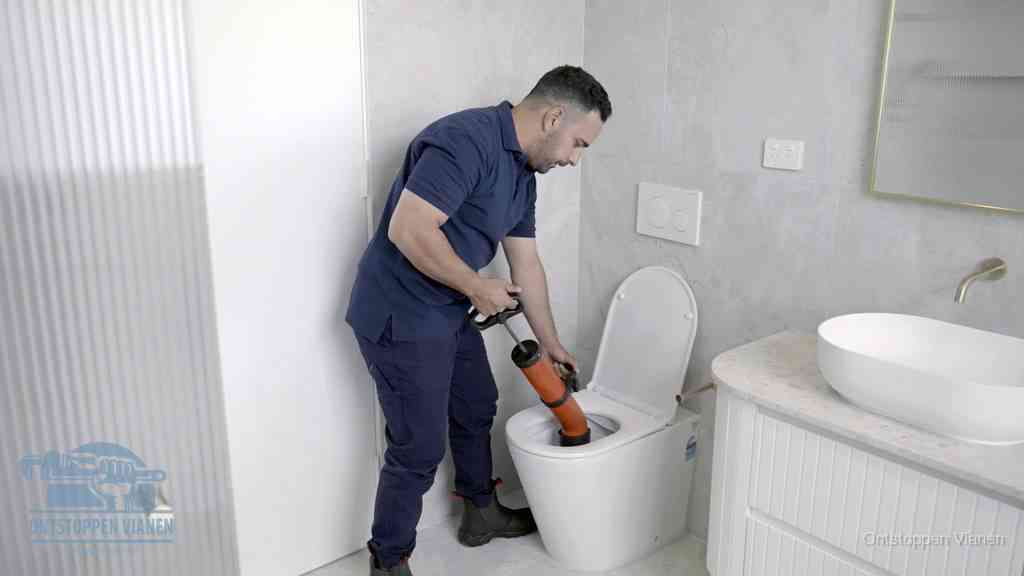 Een monteur buigt over een wandcloset en duwt met de hand een persluchtontstopper in de toiletpot om de verstopping handmatig los te maken in Vianen