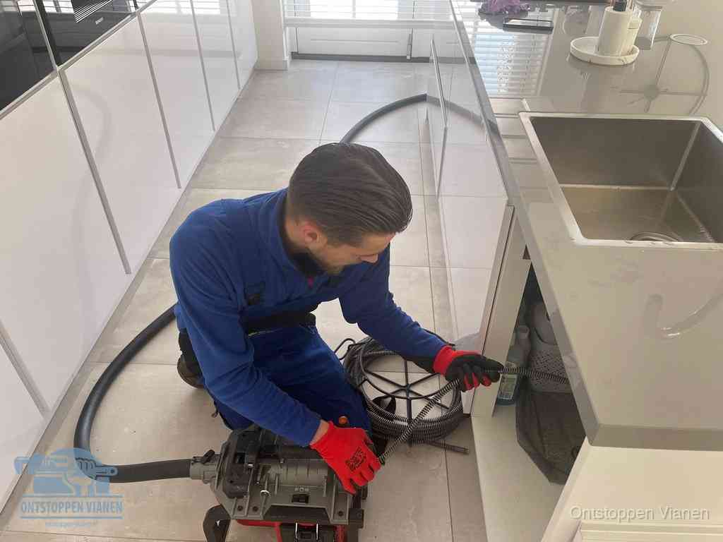 Een monteur ontstopt de keukenafvoer onder de spoelbak met een elektrische veermachine in Vianen