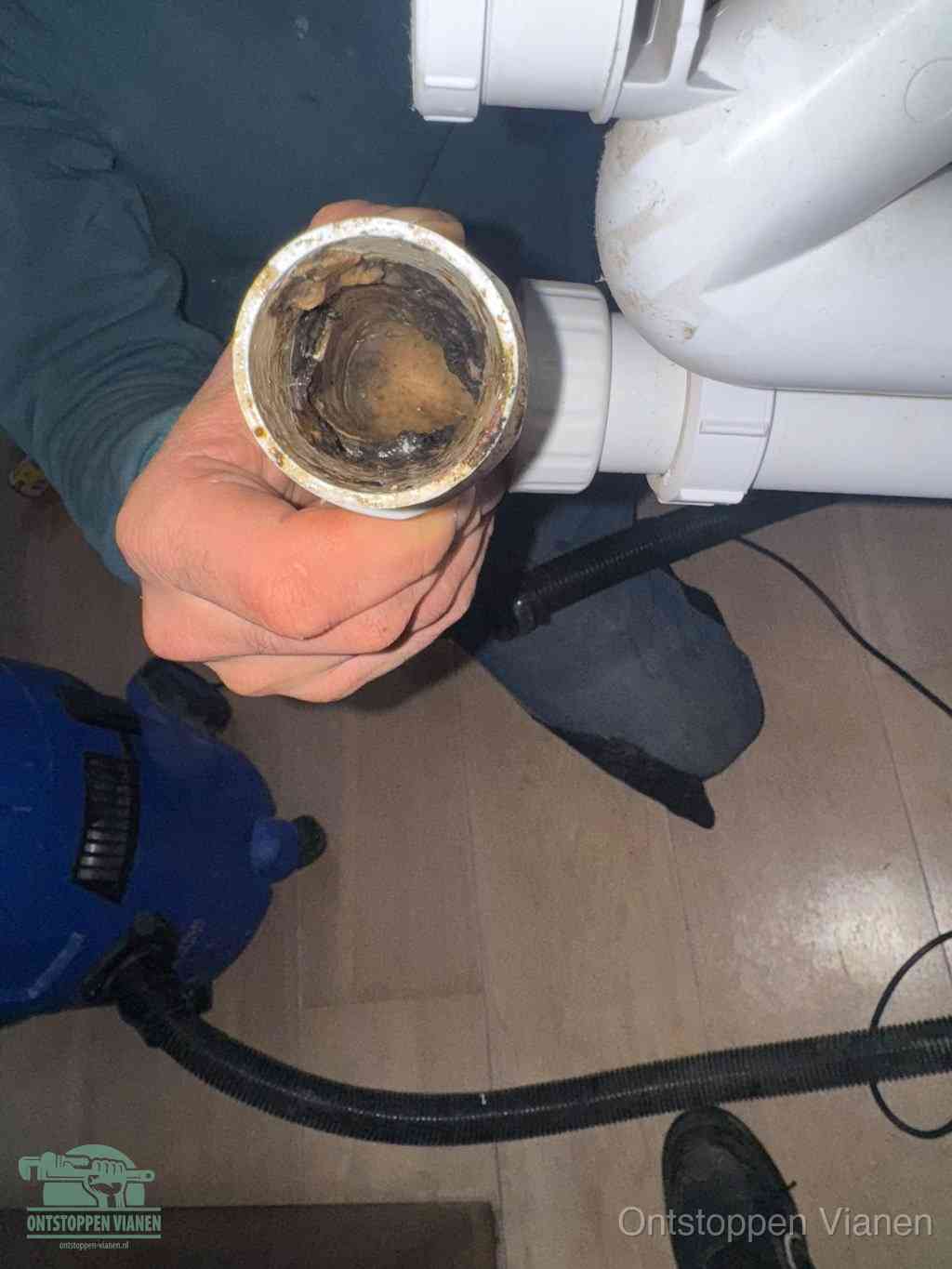 Een hand houdt een losgekoppeld PVC-afvoerbuisstuk vast dat van binnen volledig is dichtgeslibd met vet, vuil en aanslag, de meest voorkomende oorzaak van een verstopte afvoer in Vianen