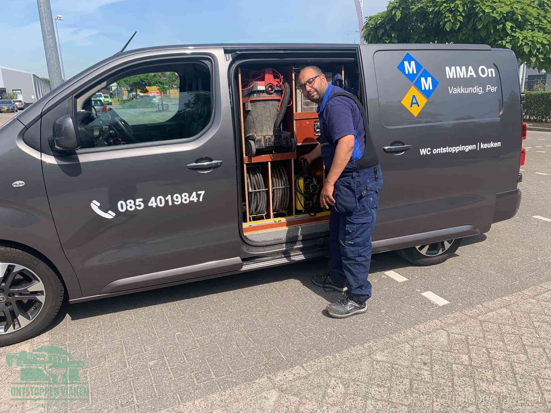 Een monteur bij de open schuifdeur van zijn bedrijfsbus op een parkeerplaats, klaar om de oorzaak van terugkerende afvoerverstoppingen aan te pakken in Vianen