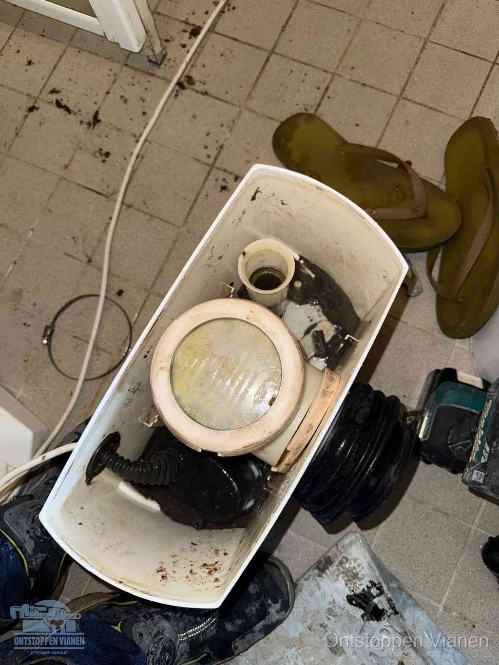 Een gedemonteerde toiletpot op de vloer met ontstoppingsveer en gereedschap ernaast, het verwijderen van een vastzittend voorwerp uit de wc in Vianen