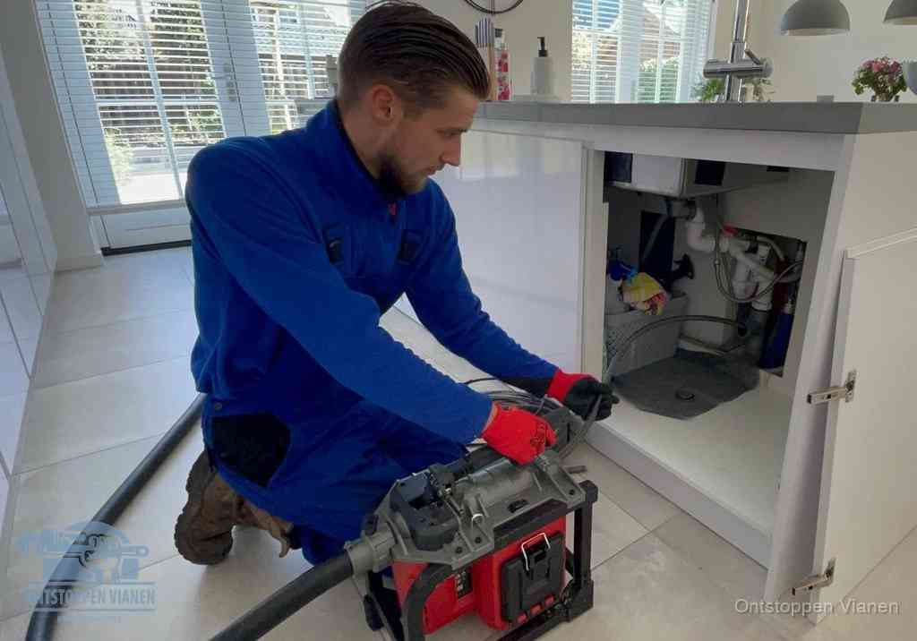 Een monteur voert een professionele elektrische ontstoppingsmachine in de afvoer onder de spoelbak tijdens het gootsteen ontstoppen in Vianen