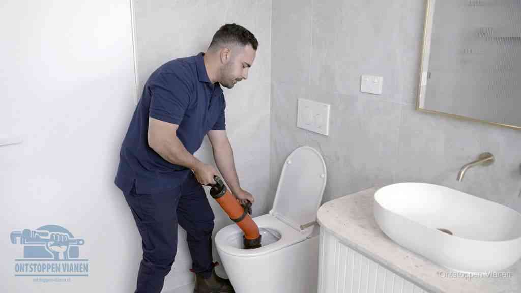 Een man gebruikt een handmatige luchtdruk-ontstopper in een modern betegeld toilet om zelf de wc te ontstoppen in Vianen